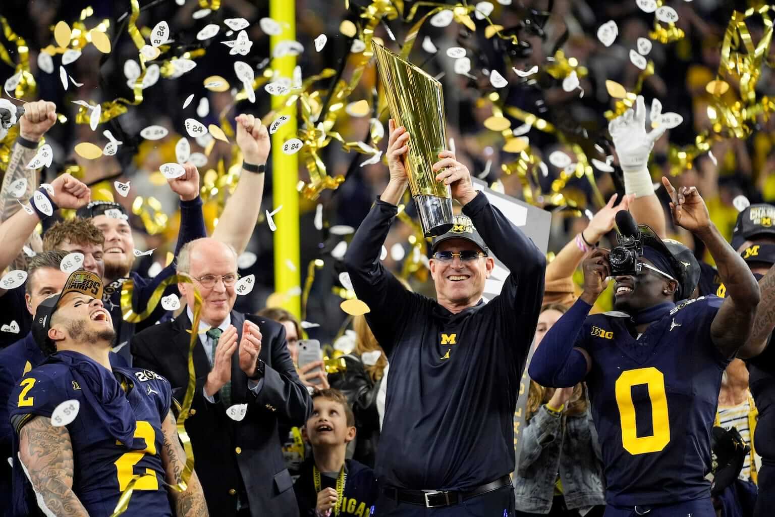 Michigan head coach Jim Harbaugh holding up the Championship trophy as confetti falls